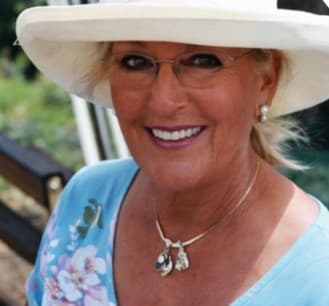 Smiling woman wearing a white sun hat, glasses, pearl earrings, and a blue floral top.